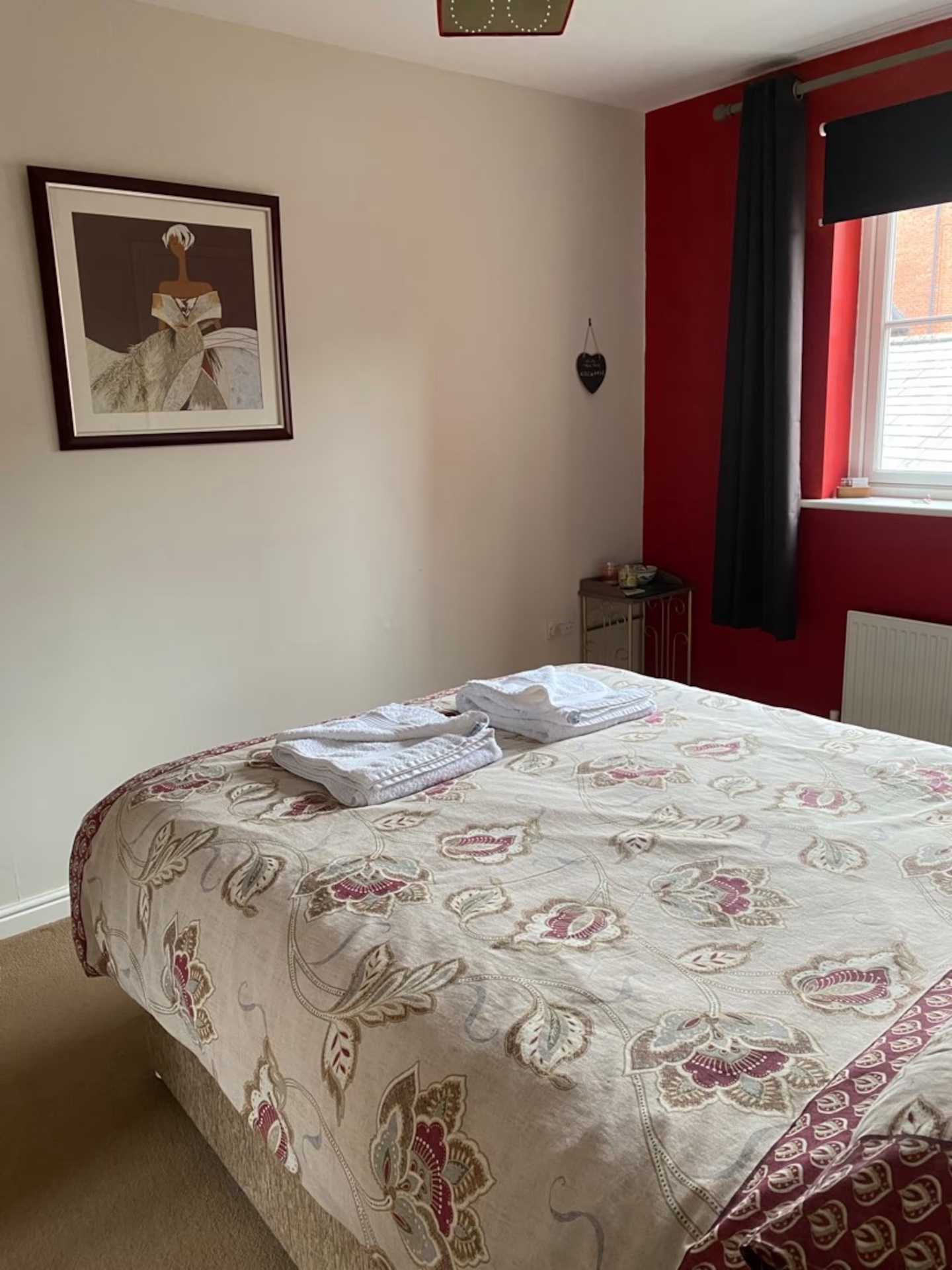 Double Room from the foot of the bed, framed artwork on the neutral wall and red accent wall by the window