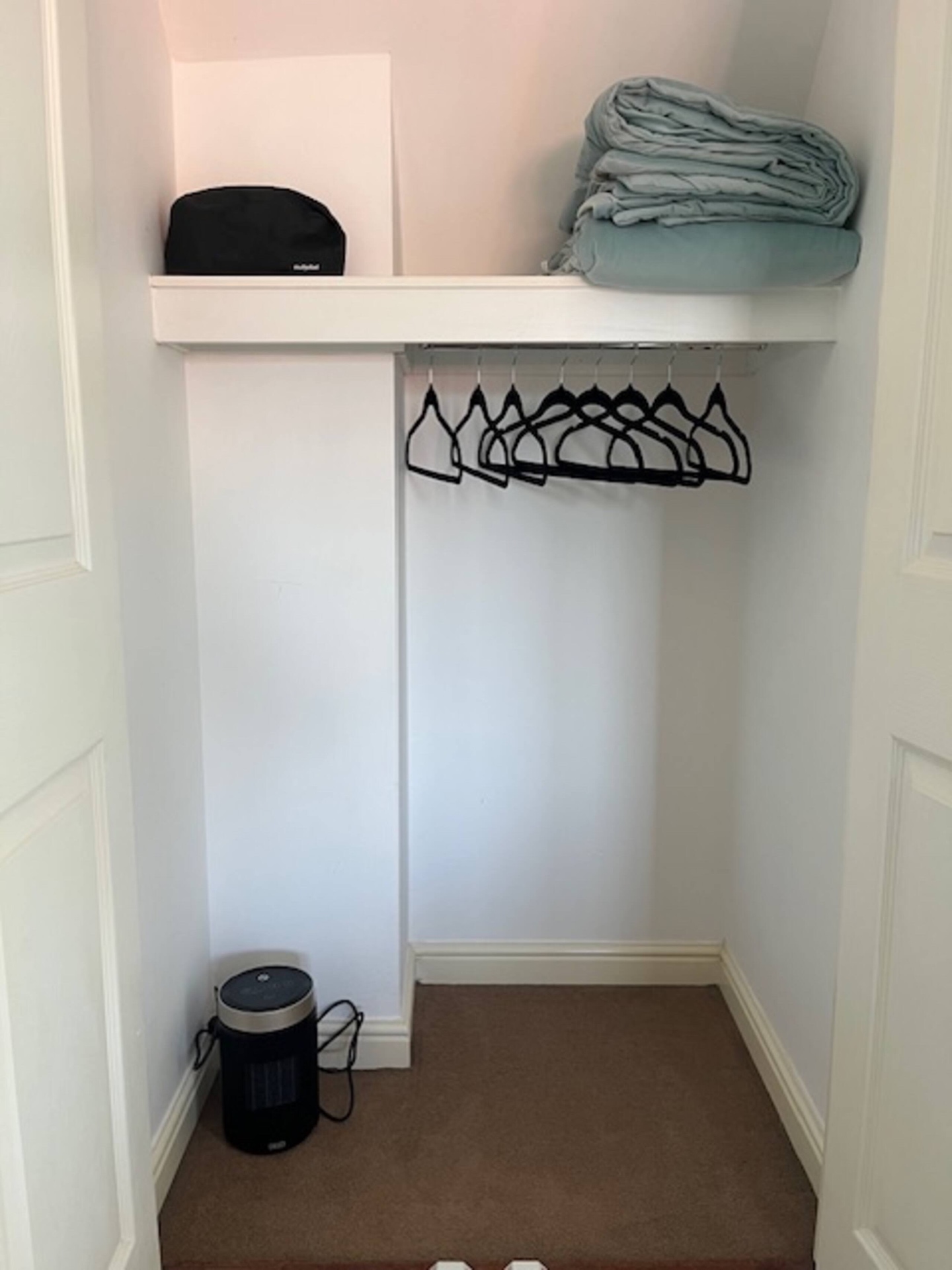 Open wardrobe with hangers, spare bedding and a portable heater