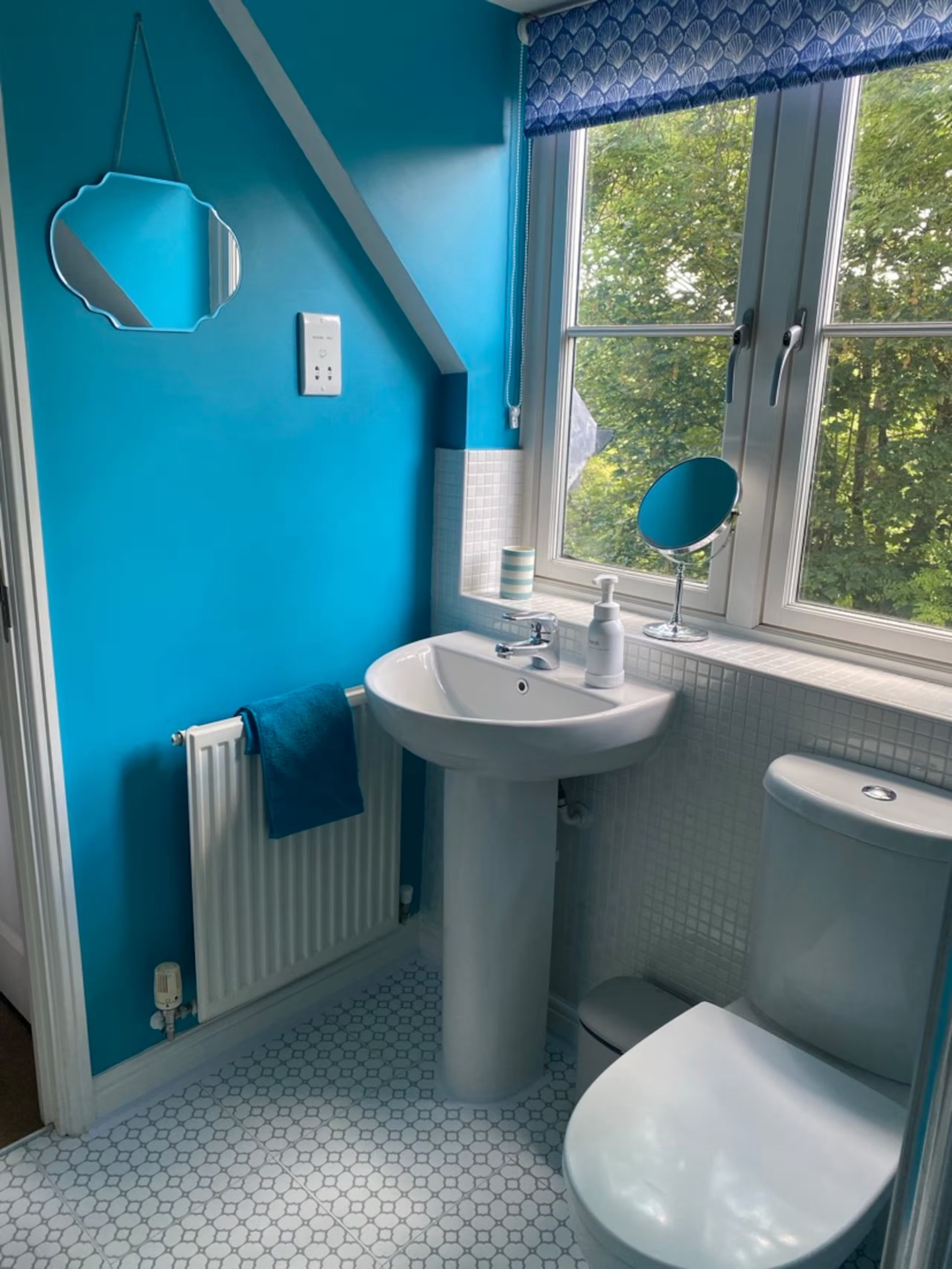 En-suite basin and WC with bright teal walls and a leafy window view