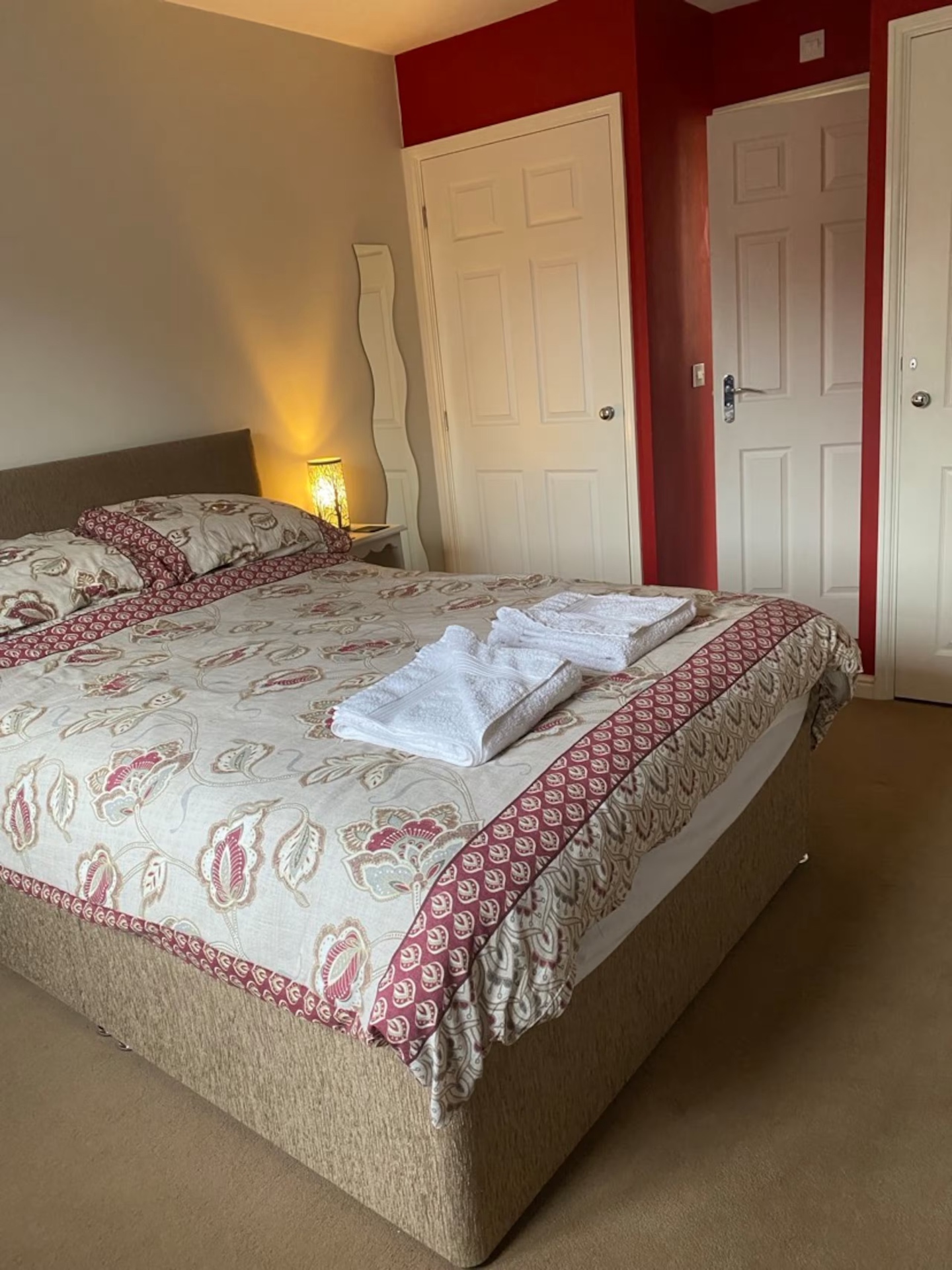 Double Room — double bed with floral throw and a warm bedside lamp against a deep red accent wall